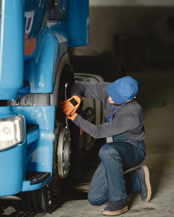 joven-trabajador-controla-rueda-mal-funcionamiento-camion-trabajo-servicio_1157-46511
